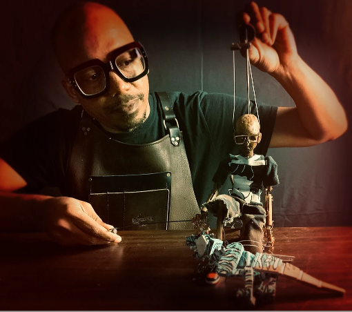 a puppeteer holding a small puppet wearing glasses.